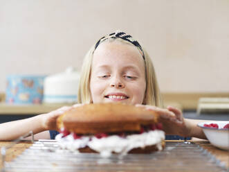 Mädchen backt einen Kuchen, drückt den oberen Biskuit am Küchentisch - CUF53533