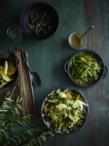 Rustikales Stilleben mit Schalen von Curryblattsalat und grünem Bohnenthoran auf dem Tisch, Draufsicht, lizenzfreies Stockfoto