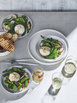 High-Key-Stillleben mit Weißweingläsern und Tellern mit Burrata-Frühlingssalat auf weißem Tisch, Draufsicht - ISF22894