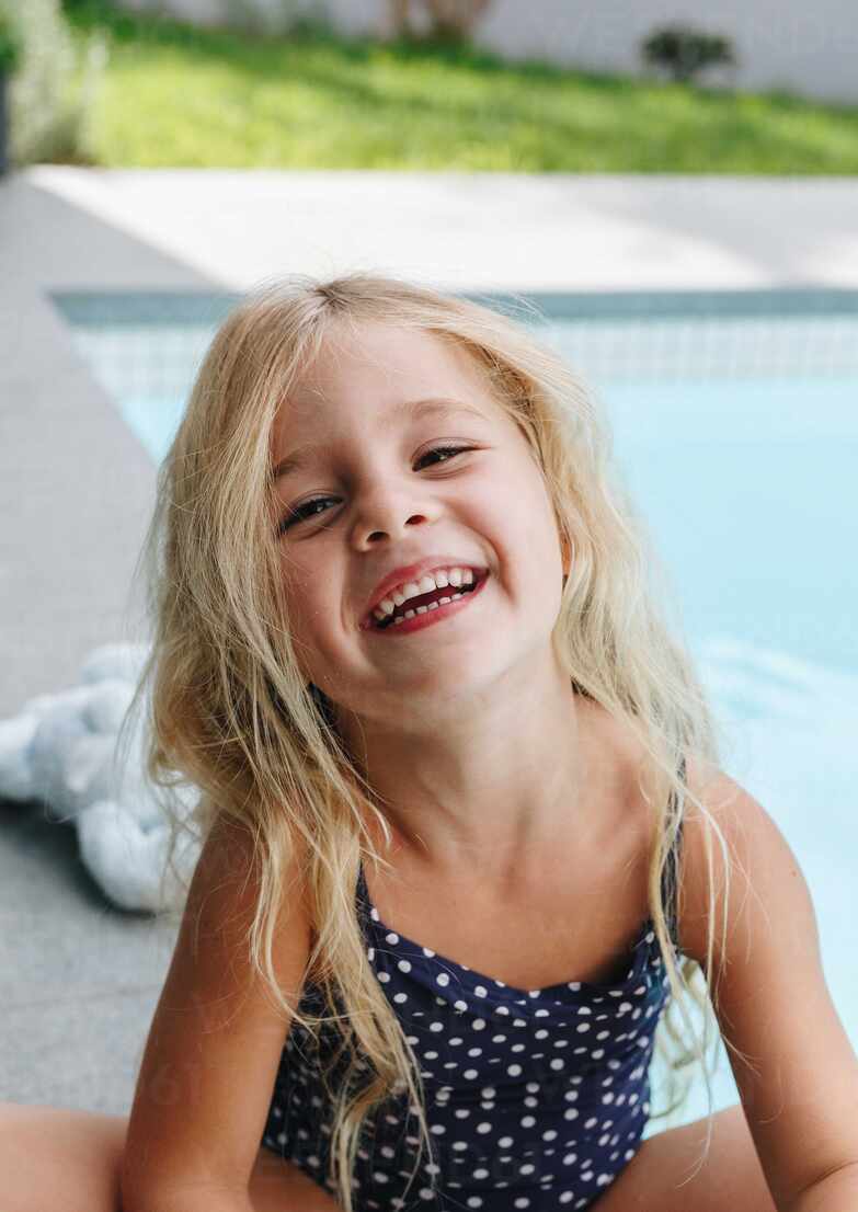 Happy little girl sitting by swimming pool stock photo