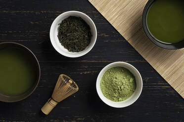 Still life of matcha tea preparation with whisk and bowls of matcha tea and tea powder, overhead view - ISF22935