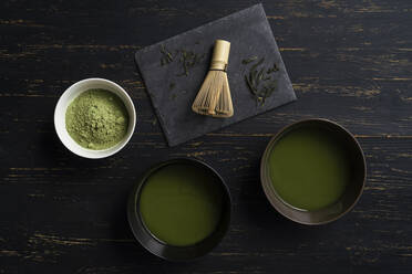 Still life of matcha tea preparation with whisk and bowls of matcha tea and tea powder, overhead view, low key - ISF22937