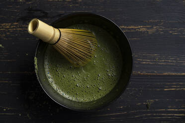 Still life of matcha tea preparation with whisk in bowl of matcha tea, overhead view, low key - ISF22939