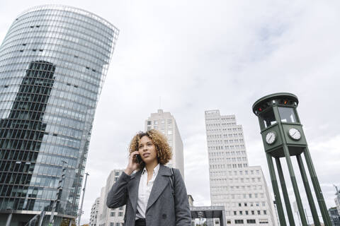 Frau am Telefon mit Bürogebäuden im Hintergrund, Berlin, Deutschland, lizenzfreies Stockfoto