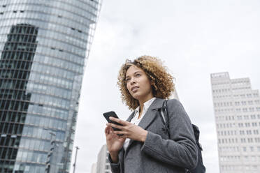 Woman holding smartphone with office buildings in background, Berlin, Germany - AHSF01265