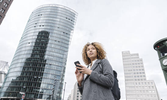 Woman holding smartphone with office buildings in background, Berlin, Germany - AHSF01266