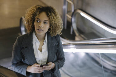 Portrait of woman with cell phone on escalator - AHSF01267