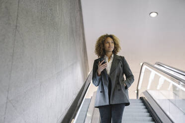 Frau hält Mobiltelefon auf Rolltreppe - AHSF01268