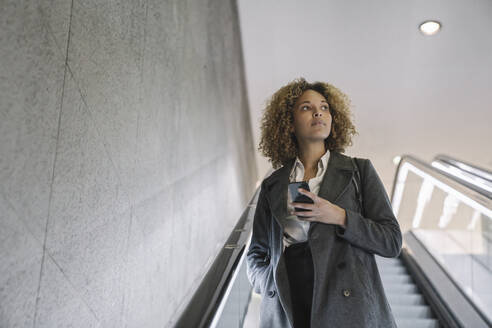 Frau hält Mobiltelefon auf Rolltreppe - AHSF01269