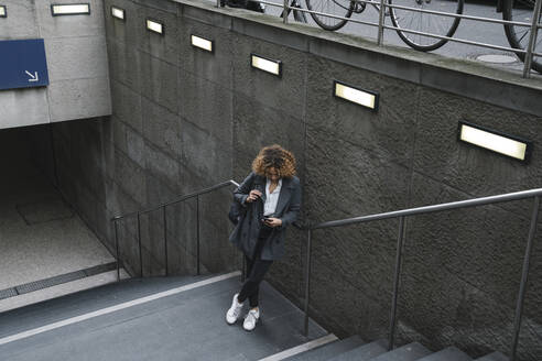 Frau mit Smartphone am Eingang einer U-Bahn-Station, Berlin, Deutschland - AHSF01288