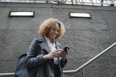 Lächelnde Frau mit Smartphone am Eingang einer U-Bahn-Station, Berlin, Deutschland - AHSF01292