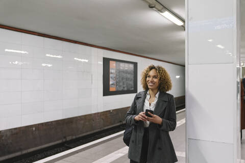 Smiling woman with cell phone waiting in subway station stock photo