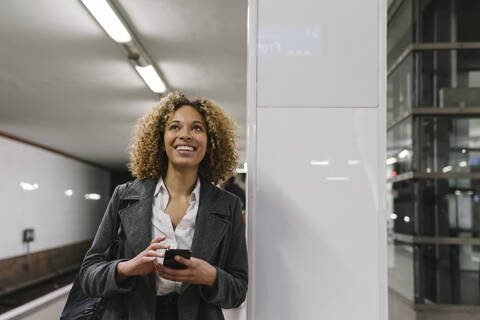 Glückliche Frau mit Handy wartet in der U-Bahn-Station, lizenzfreies Stockfoto