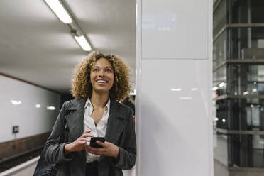 Glückliche Frau mit Handy wartet in der U-Bahn-Station - AHSF01294