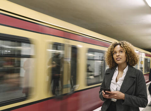 Woman with cell phone in subway station as the train comes in stock photo