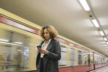 Frau benutzt Mobiltelefon in der U-Bahn-Station, als der Zug einfährt - AHSF01296