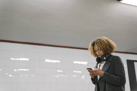 Frau benutzt Smartphone in U-Bahn-Station, lizenzfreies Stockfoto