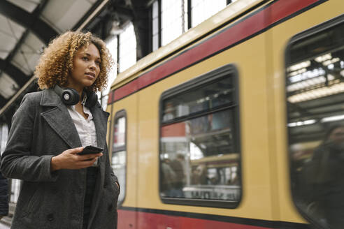Frau mit Handy in der U-Bahn-Station, als der Zug einfährt - AHSF01304