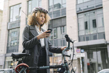 Woman with bicycle and smartphone in the city, Berlin, Germany - AHSF01317