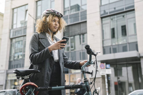 Frau mit Fahrrad und Smartphone in der Stadt, Berlin, Deutschland - AHSF01317