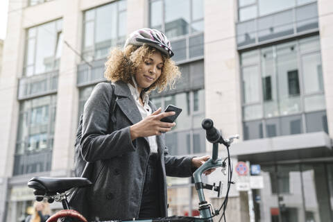 Woman with bicycle and smartphone in the city, Berlin, Germany stock photo