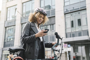 Frau mit Fahrrad und Smartphone in der Stadt, Berlin, Deutschland - AHSF01318