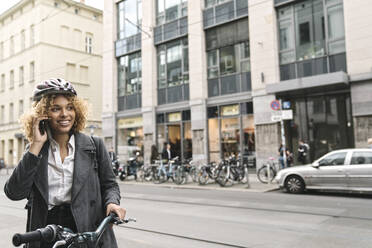 Lächelnde Frau mit Fahrrad beim Telefonieren in der Stadt, Berlin, Deutschland - AHSF01321