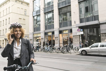 Smiling woman with bicycle talking on the phone in the city, Berlin, Germany - AHSF01321