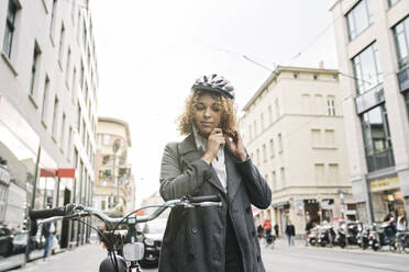 Frau beim Aufsetzen des Fahrradhelms in der Stadt, Berlin, Deutschland - AHSF01323