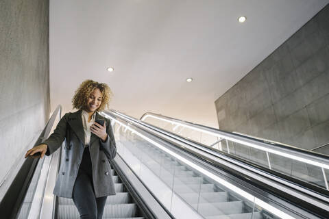 Lächelnde Frau, die auf einer Rolltreppe ein Mobiltelefon benutzt, lizenzfreies Stockfoto