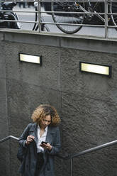 Frau mit Smartphone am Eingang einer U-Bahn-Station, Berlin, Deutschland - AHSF01341