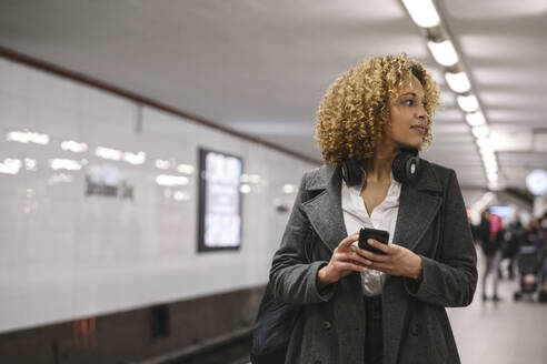 Frau mit Mobiltelefon wartet in der U-Bahn-Station - AHSF01342