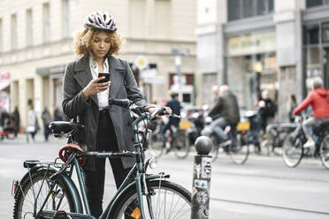 Woman with bicycle and smartphone in the city, Berlin, Germany - AHSF01347