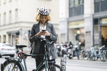 Frau mit Fahrrad und Smartphone in der Stadt, Berlin, Deutschland - AHSF01349