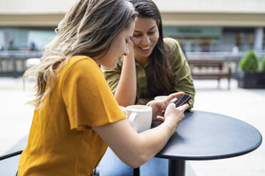 Lesbisches Paar mit Smartphone in einem Straßencafé in der Stadt, London, UK - FBAF00968