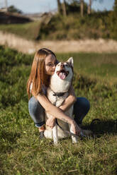 Happy young woman hugging her dog on a meadow - MAUF03081