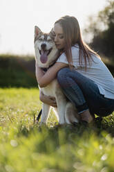 Young woman hugging her dog on a meadow - MAUF03083