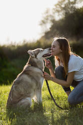 Young woman nose to nose with her dog on a meadow - MAUF03090