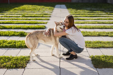 Happy young woman cuddling her dog outdoors - MAUF03095