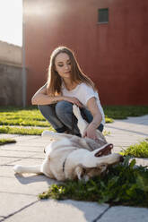 Portrait of young woman stroking her dog outdoors in the evening - MAUF03100