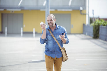 Casual mature man using smartphone walking on parking deck - UUF19713