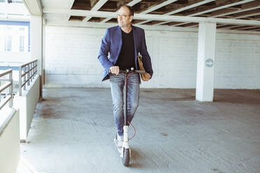 Mature businessman riding e-scooter in parking garage - UUF19715