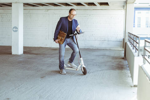 Mature businessman with e-scooter and smartphone in parking garage stock photo
