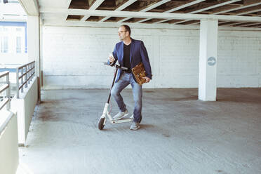 Älterer Geschäftsmann mit E-Roller und Smartphone im Parkhaus - UUF19717