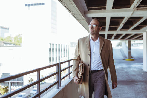 Mature businessman with briefcase walking on parking deck - UUF19719