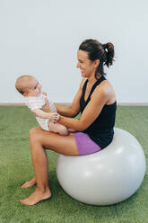Junge Mutter und Baby trainieren auf einem Fitnessball - MPPF00289