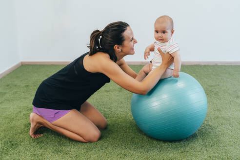 Junge Mutter und Baby trainieren auf einem Fitnessball - MPPF00290