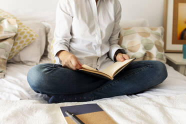 Close-up of woman with book sitting on bed at home - VABF02334