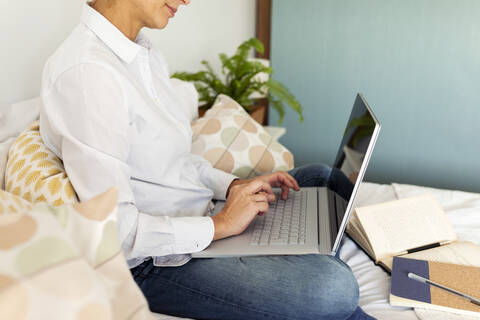 Mature woman sitting on bed at home using laptop stock photo