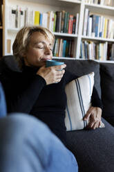 Ältere Frau entspannt sich auf der Couch zu Hause und trinkt aus einer Tasse - VABF02375